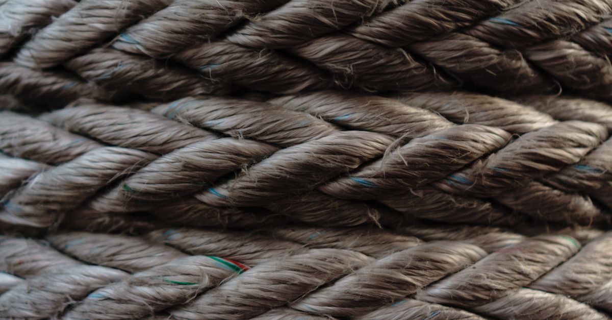 Mains qui tressent une corde de fortune avec des fibres végétales
