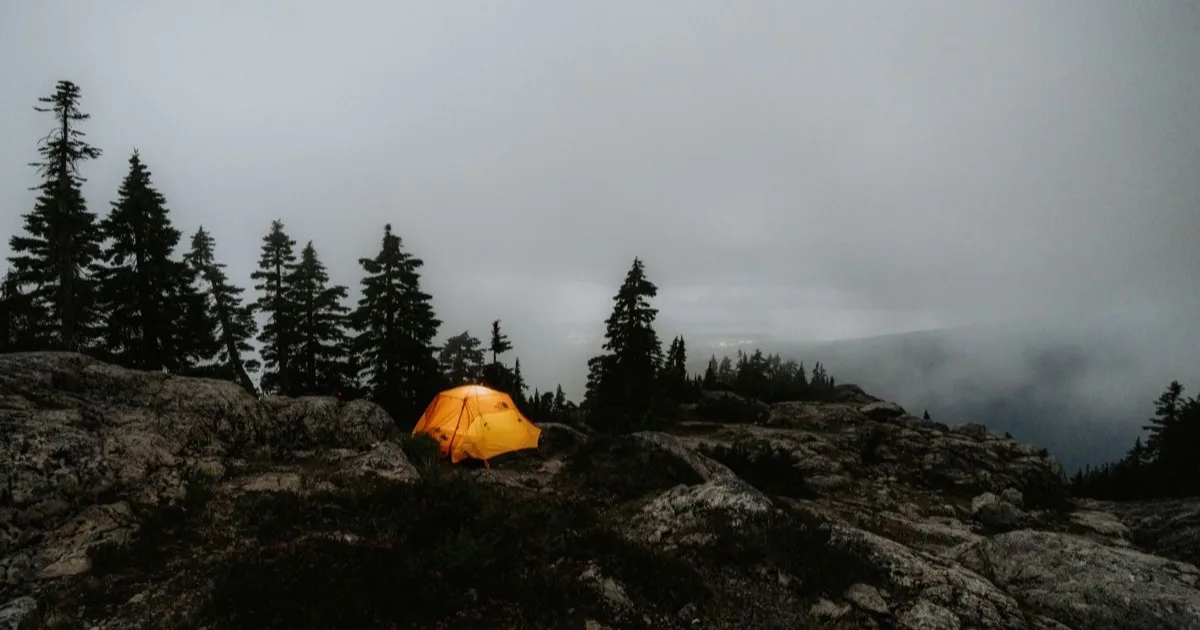 Bivouac légal en montagne : tente orange dans la brume parmi les pins