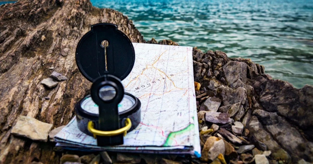 How to use a compass: lensatic compass on a hiking map beside a lake